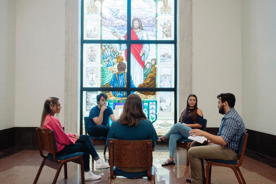 部 students sit in a circle and study the bible in a chapel.